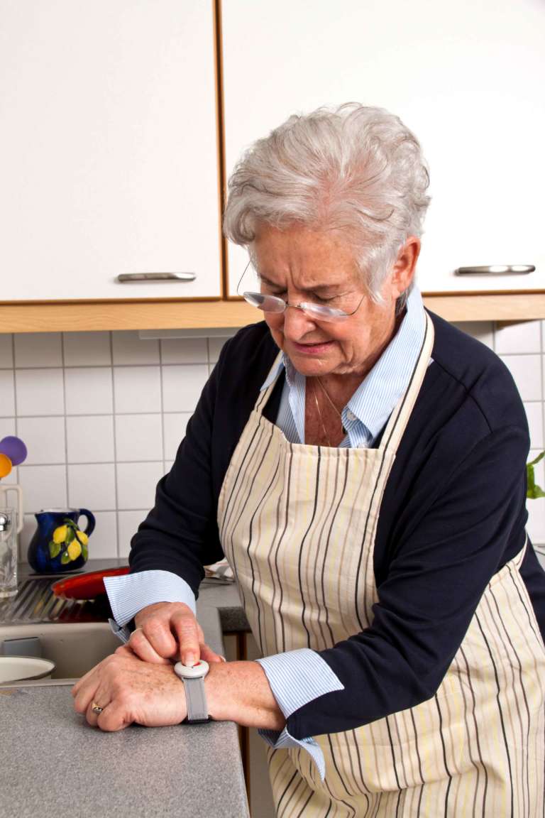 Fester Hausnotruf. Seniorin mit Notrufarmband zu Hause.